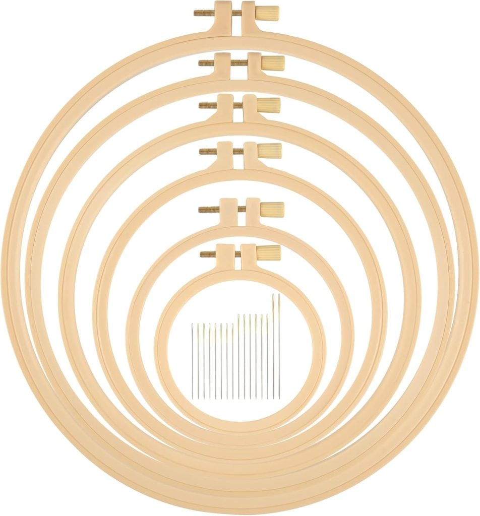 Six wooden embroidery hoops of varying sizes stacked concentrically, with a set of embroidery needles placed in the center.