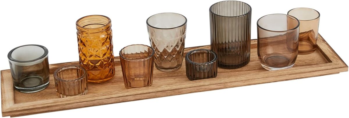 A wooden tray holding ten assorted glass candle holders in various colors, shapes, and sizes.