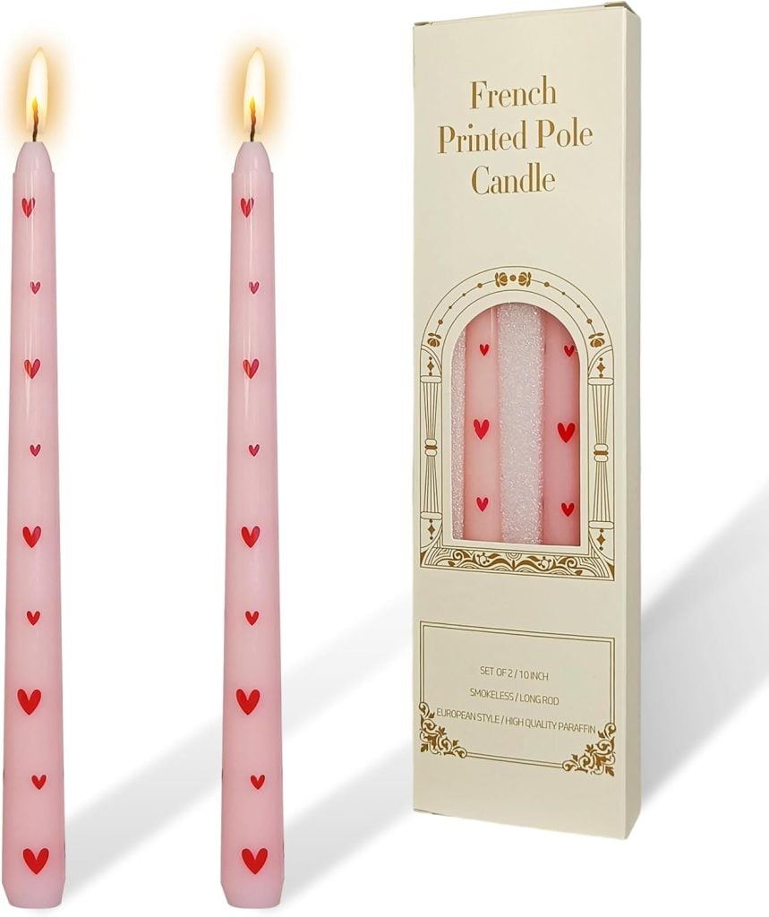 Two pink taper candles with red heart prints stand next to a cream-colored box labeled "French Printed Pole Candle," which displays two matching candles inside.