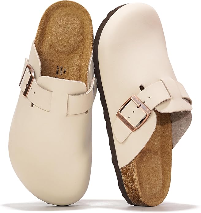 A pair of beige slip-on clogs with adjustable metal buckles and cork insoles, positioned upright on a white background.