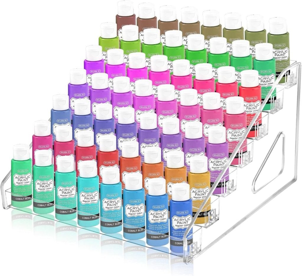 Acrylic paint bottles in various colors are organized on a clear, three-tiered display rack.