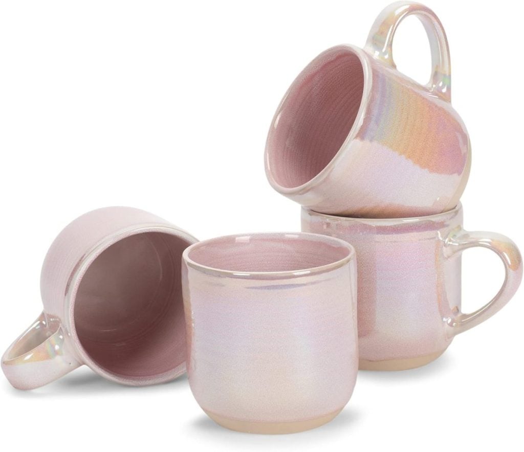Four iridescent pink ceramic mugs are stacked and arranged on a white surface, two upright and two on their sides, perfect for adding to your list of Things To Do This Year&mdash;like elevating your kitchen style.