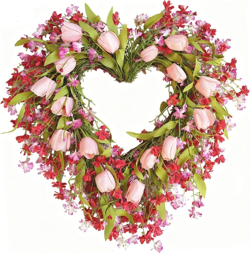A heart-shaped wreath made of pink tulips, red and pink small flowers, and green leaves on a white background.