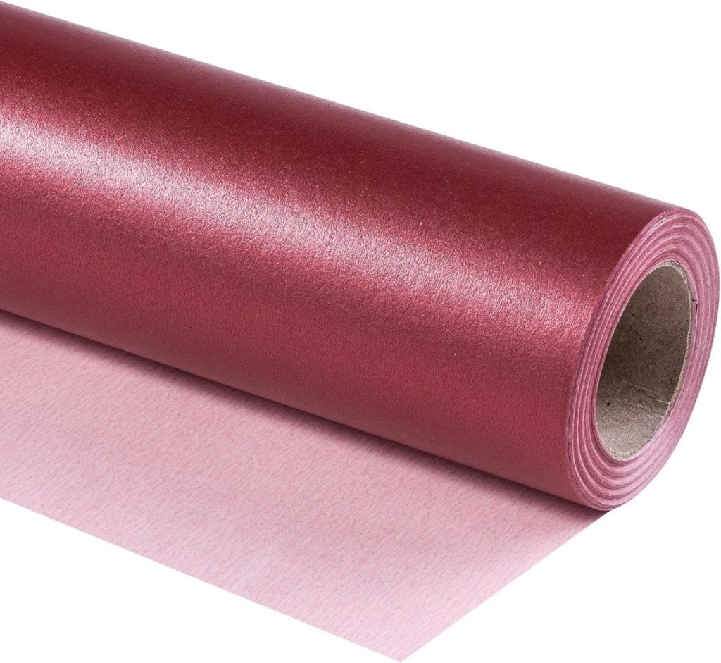 A roll of metallic pink wrapping paper partially unrolled, showing its smooth, reflective surface and cardboard core.