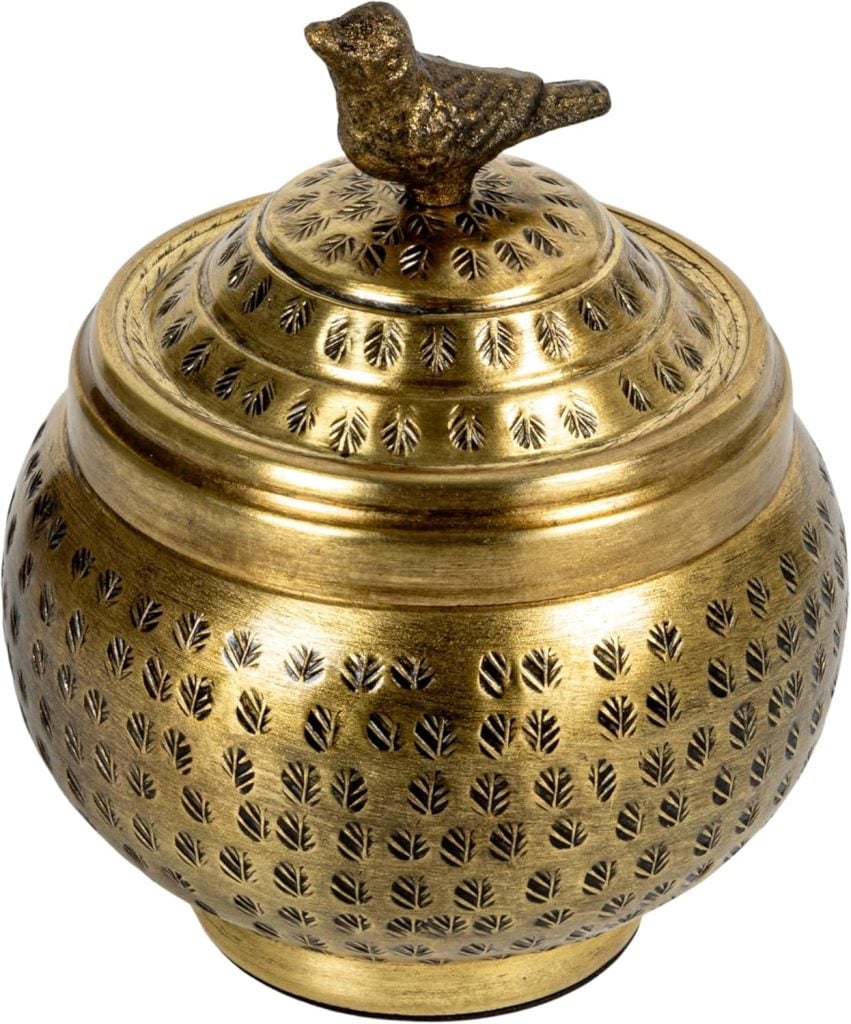 A round, gold-colored metal container with leaf-like patterns and a lid topped by a small bird figurine.