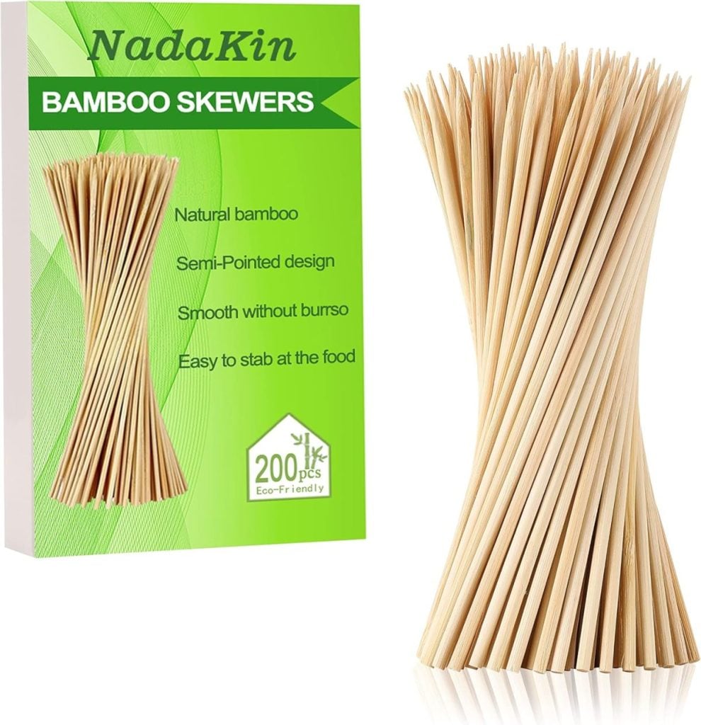 A box labeled "NadaKin Bamboo Skewers" next to a bundle of bamboo skewers; the packaging highlights features like natural bamboo and semi-pointed design.