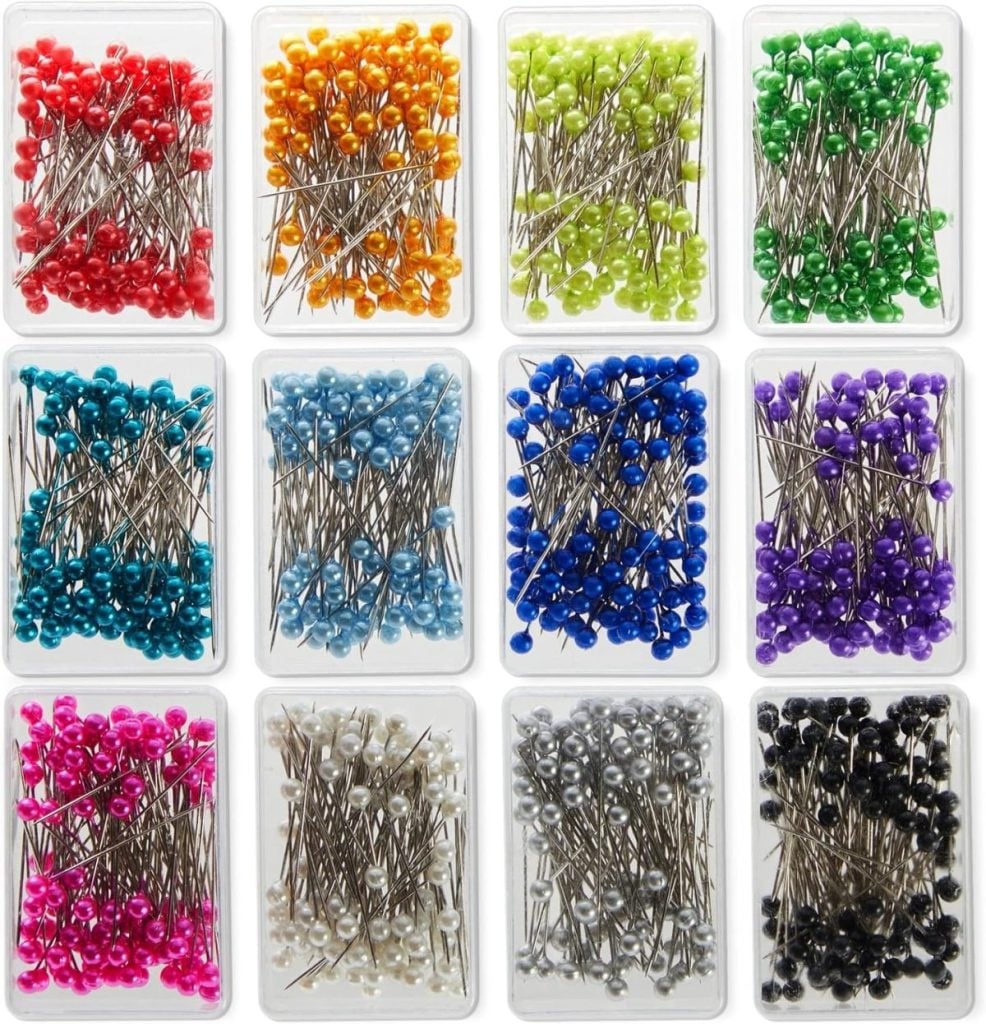 Twelve clear boxes, each filled with sewing pins topped with round heads, organized by color in a 3x4 grid; colors include red, orange, yellow, green, blue, purple, pink, white, gray, and black.