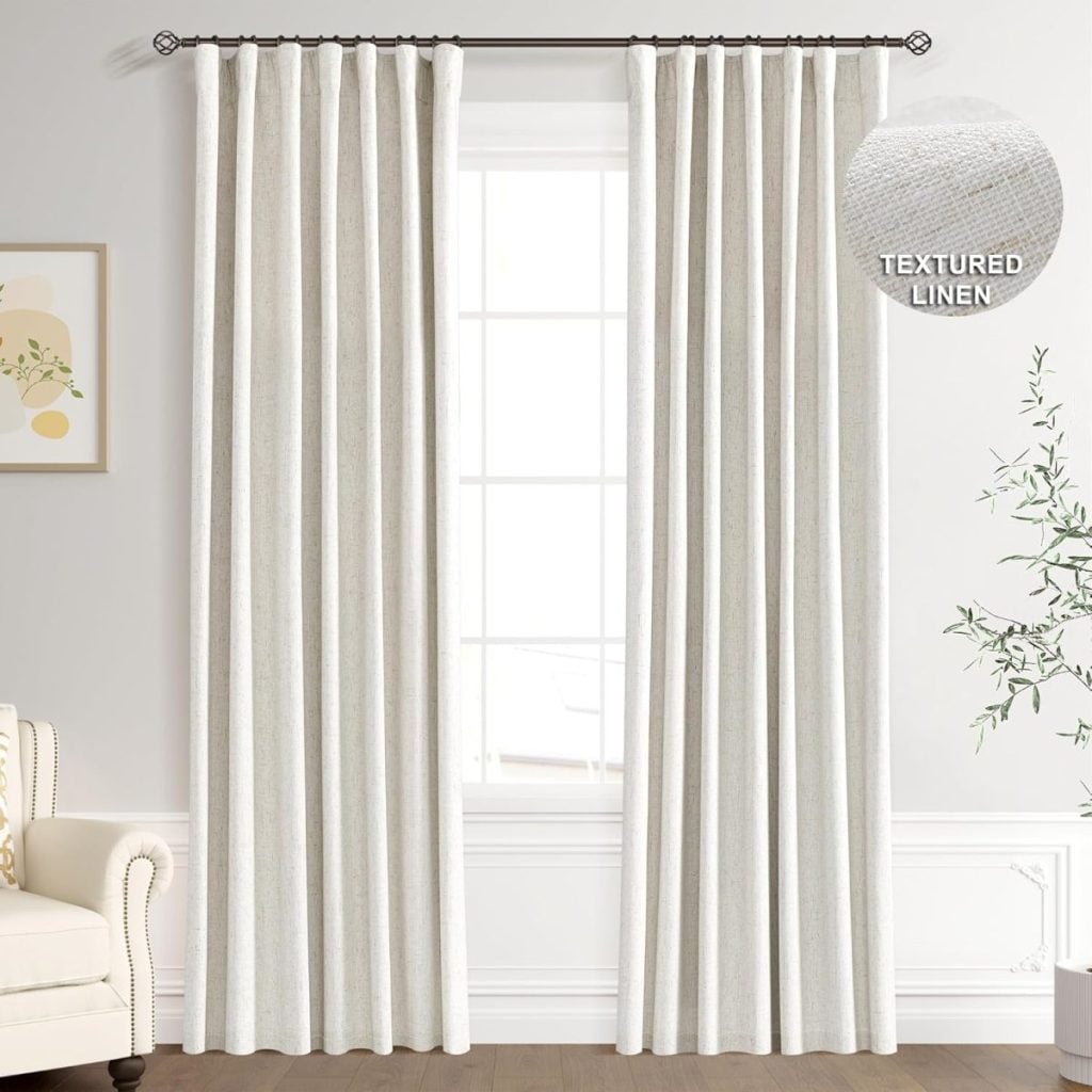 White textured linen curtains hang from a black rod in front of a large window in a bright, neutral living room. A close-up inset shows the fabric texture.
