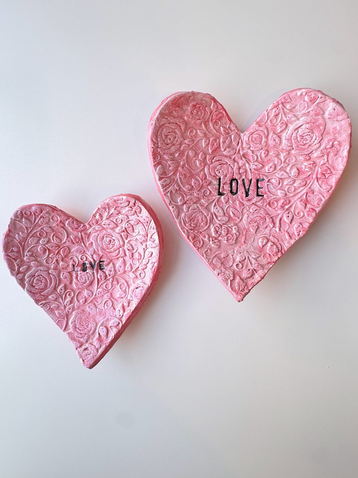 Two pink, textured clay hearts with embossed floral patterns; the smaller heart reads "You," and the larger heart reads "Love.