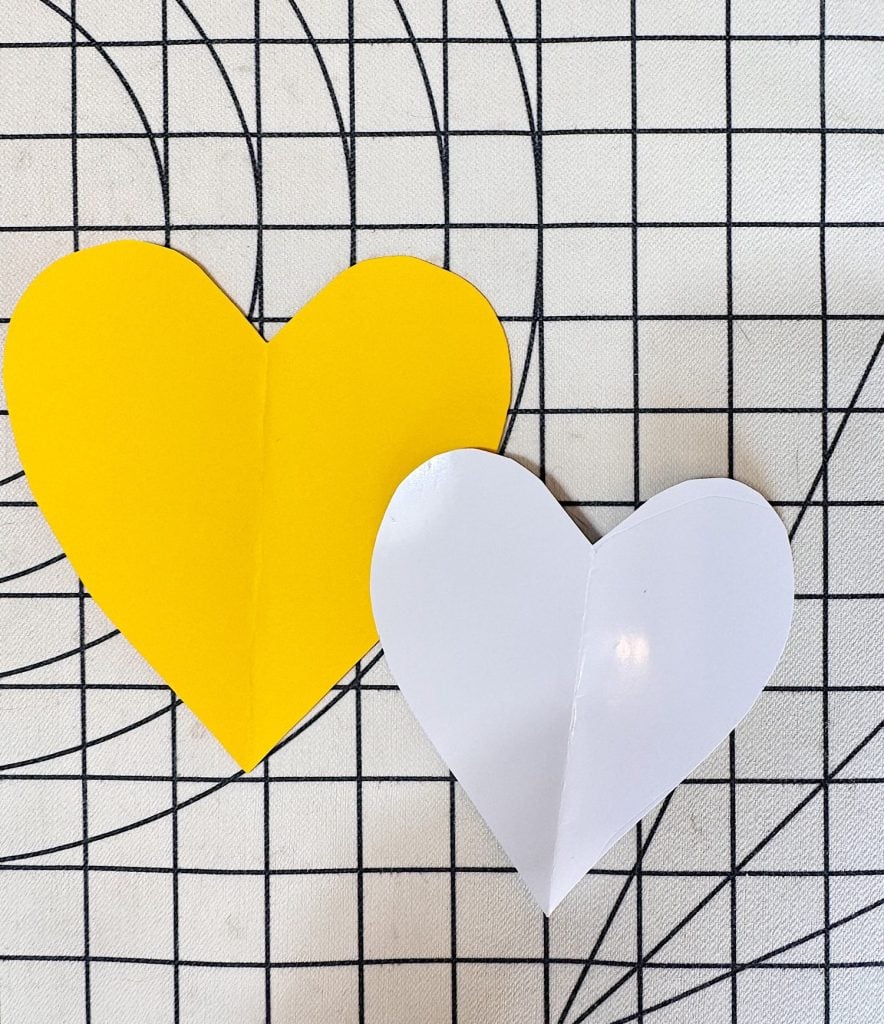 Two paper hearts, one yellow and one white, placed on a black grid patterned background.
