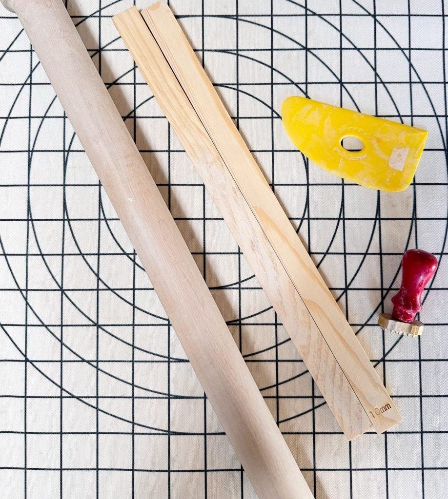 A rolling pin, two wooden dowels, a yellow dough scraper, and a red-handled tool on a gridded surface.