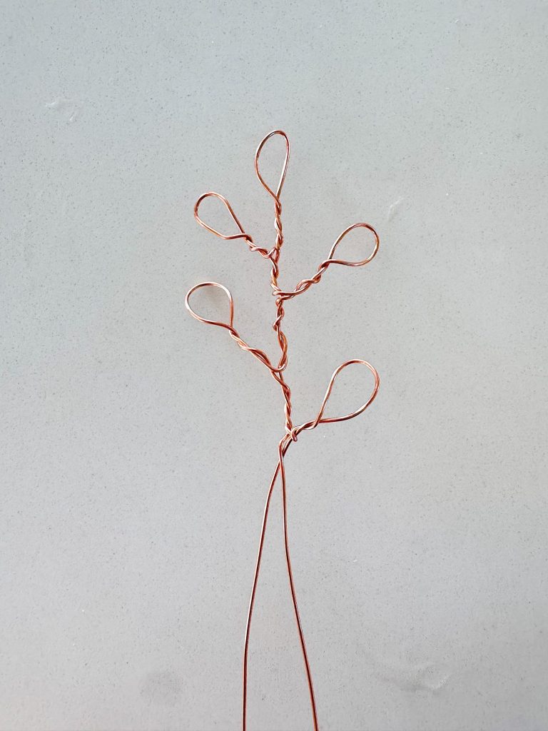 A piece of copper wire twisted into a simple tree-like shape with five looped branches against a plain background.