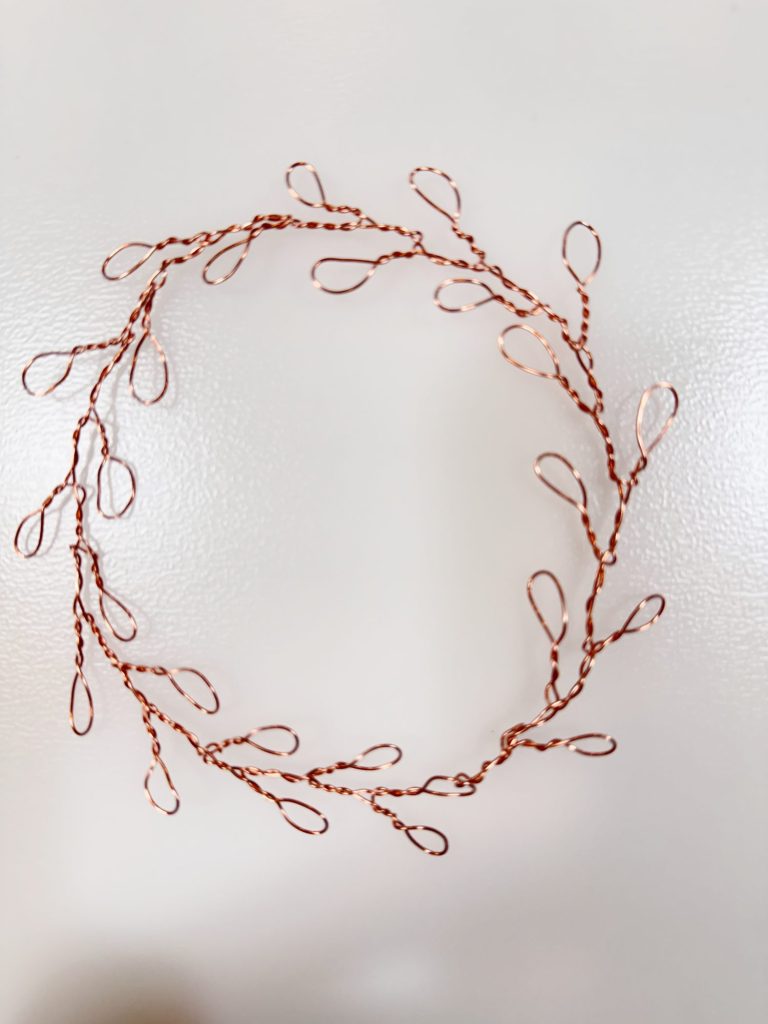 A circular arrangement of twisted copper wire with evenly spaced loops branching outward, displayed on a plain white surface.