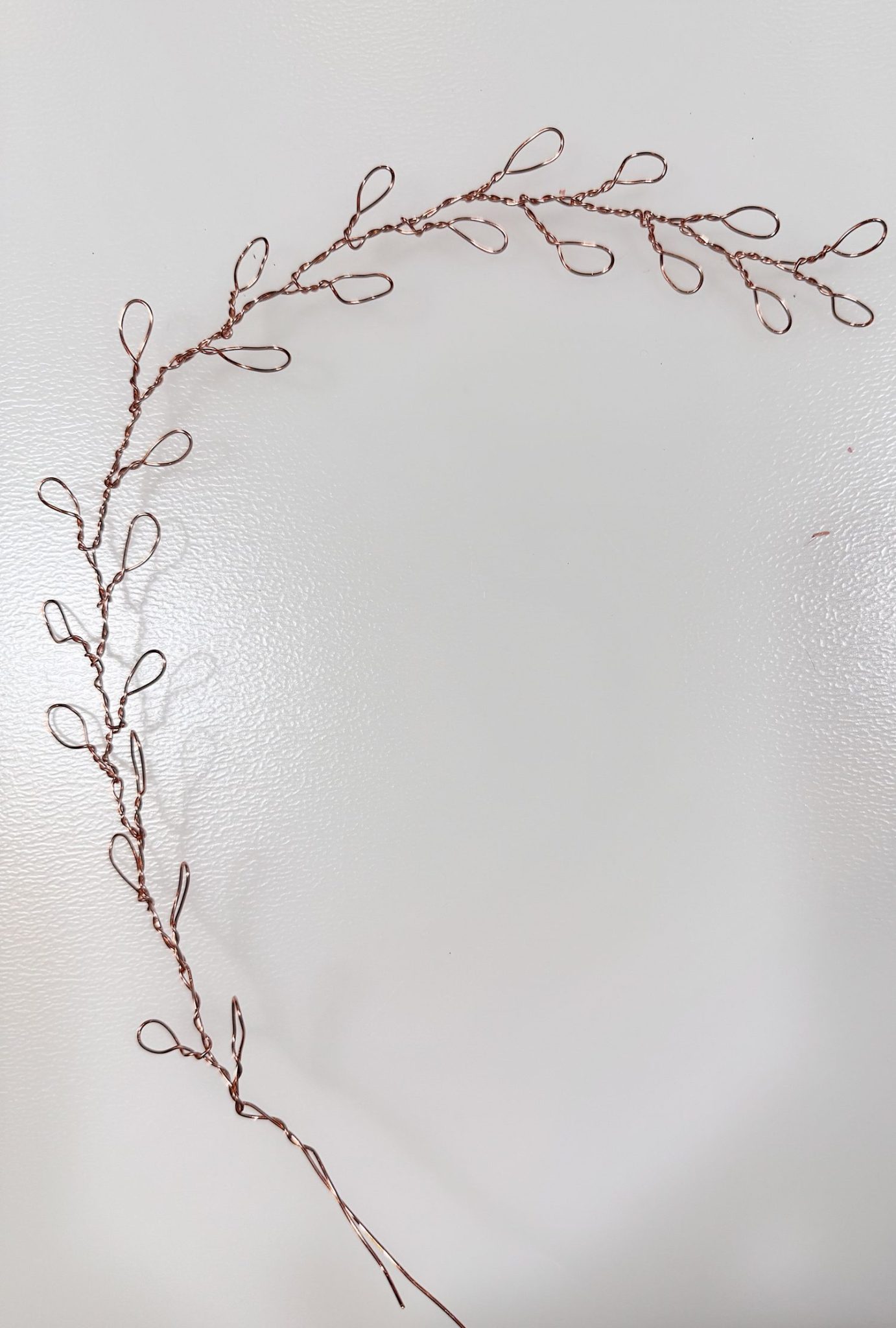 A handcrafted wire branch with looped wire leaves arranged in a curved, semi-circular shape on a white background.