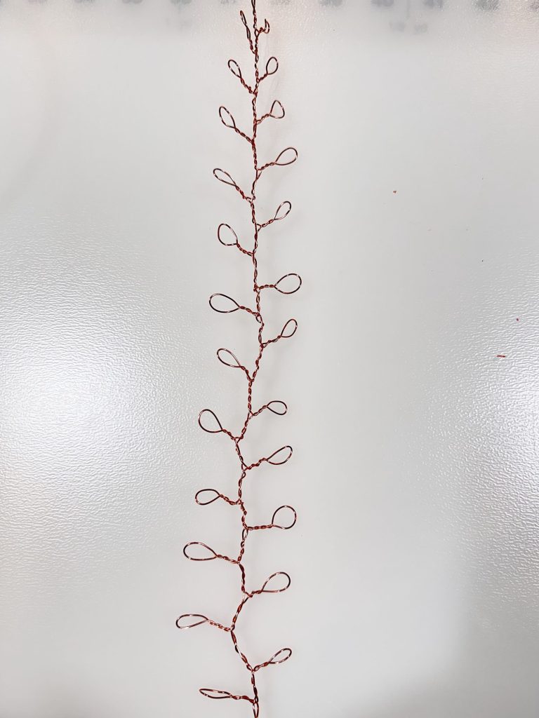 A length of thin wire twisted into a vertical line with evenly spaced loops branching out on both sides, placed on a white surface.