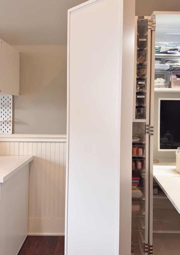 A white cabinet with a closed door is in the center, partially revealing organized storage shelves with various items in clear containers to the right.