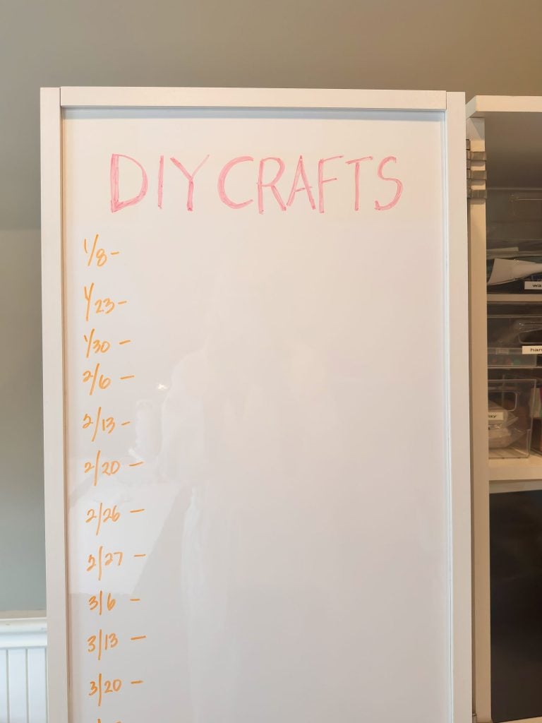 A whiteboard labeled "DIY Crafts" in pink with a numbered list in orange along the left side; shelves with storage containers are partially visible to the right.