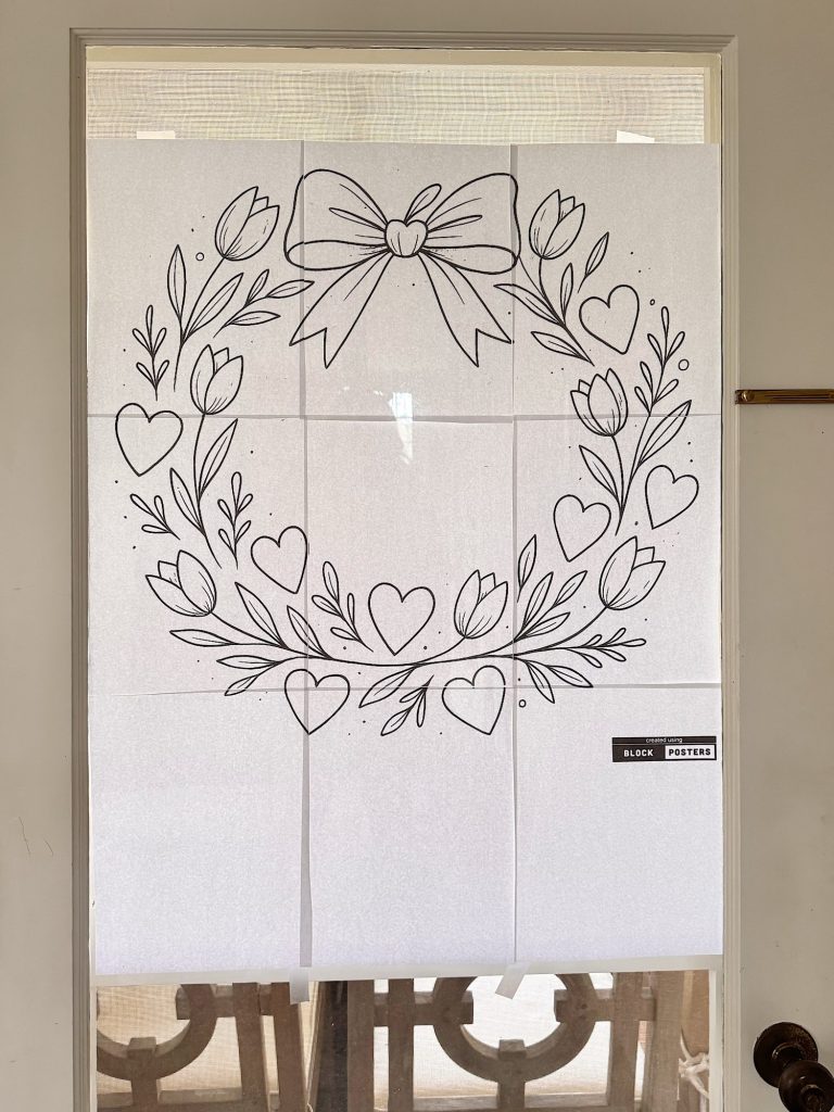 A black and white line drawing of a wreath with tulips, leaves, hearts, and a large bow, printed on multiple sheets of paper and taped to a glass door.