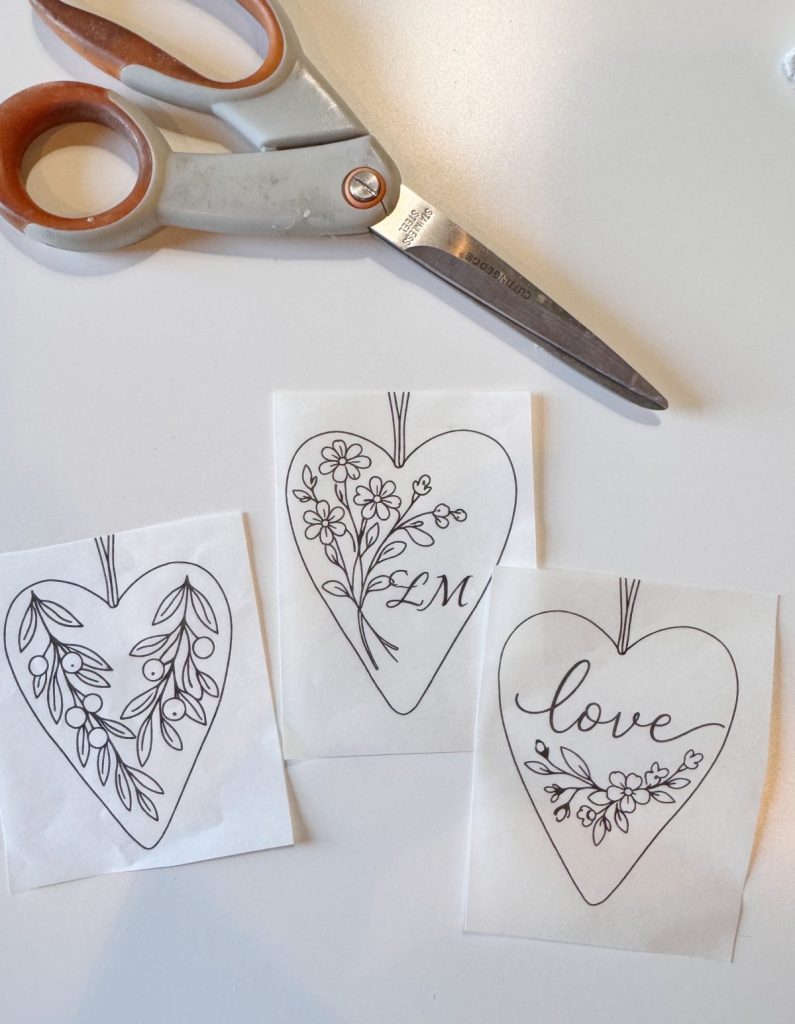 A pair of scissors and three heart-shaped paper designs with floral patterns; one is labeled "LM" and another says "love.
