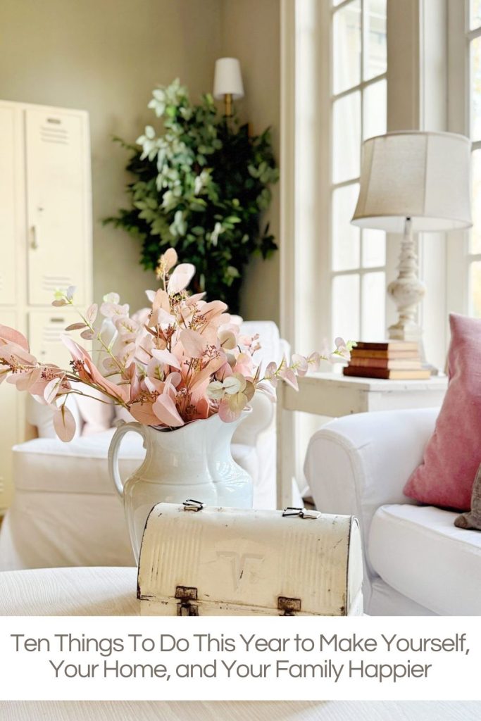 A bright living room with white furniture, a vase of pink flowers, a white metal box on a table, and a stack of books, with text about happiness tips at the bottom.