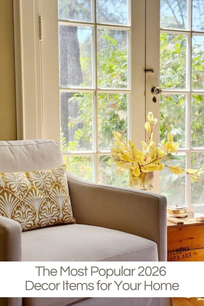 A modern armchair with a patterned pillow sits by a glass door; a vase with yellow foliage decorates a small table. Text reads: "The Most Popular 2026 Decor Items for Your Home.