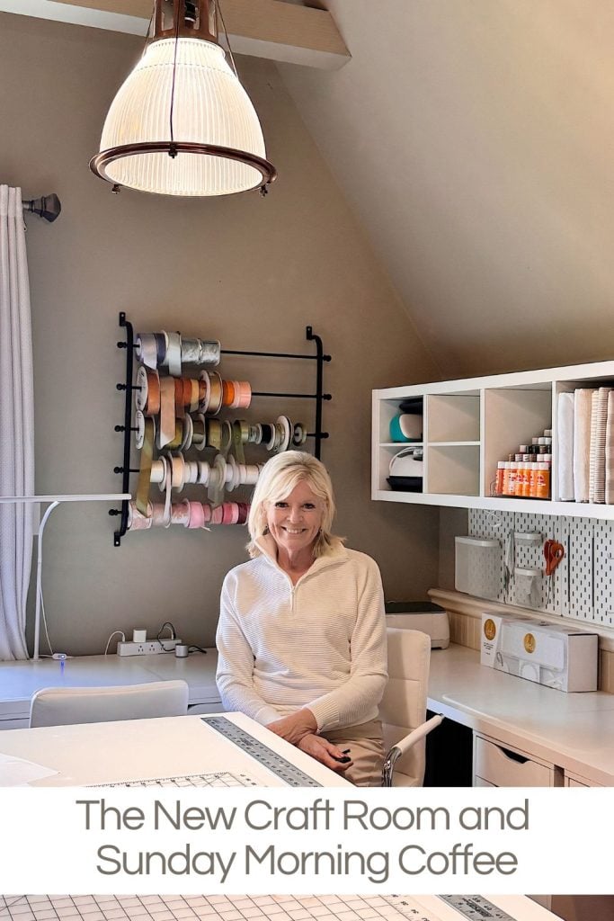 A woman sits at a white desk in a craft room with shelves, craft supplies, and a wall-mounted ribbon rack. Text at the bottom reads, "The New Craft Room and Sunday Morning Coffee.
