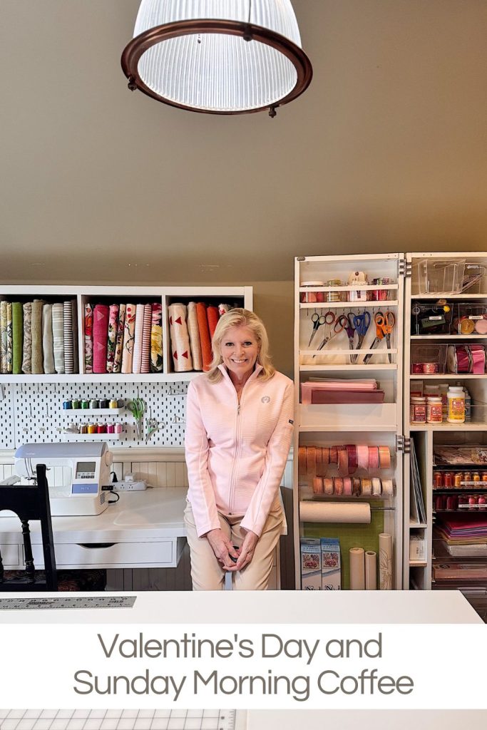 A woman stands and smiles in a craft room with organized shelves of fabric, ribbon, and supplies beneath a hanging light. Text reads: "Valentine's Day and Sunday Morning Coffee.