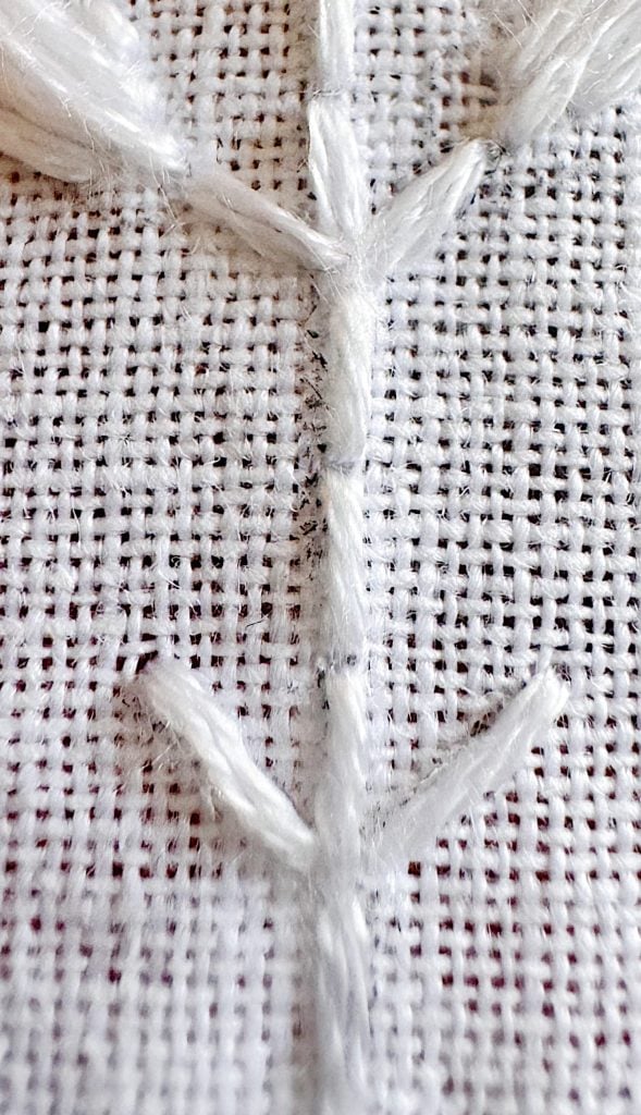 Close-up of a white embroidered pattern resembling a stem with branches on a coarse woven fabric background.