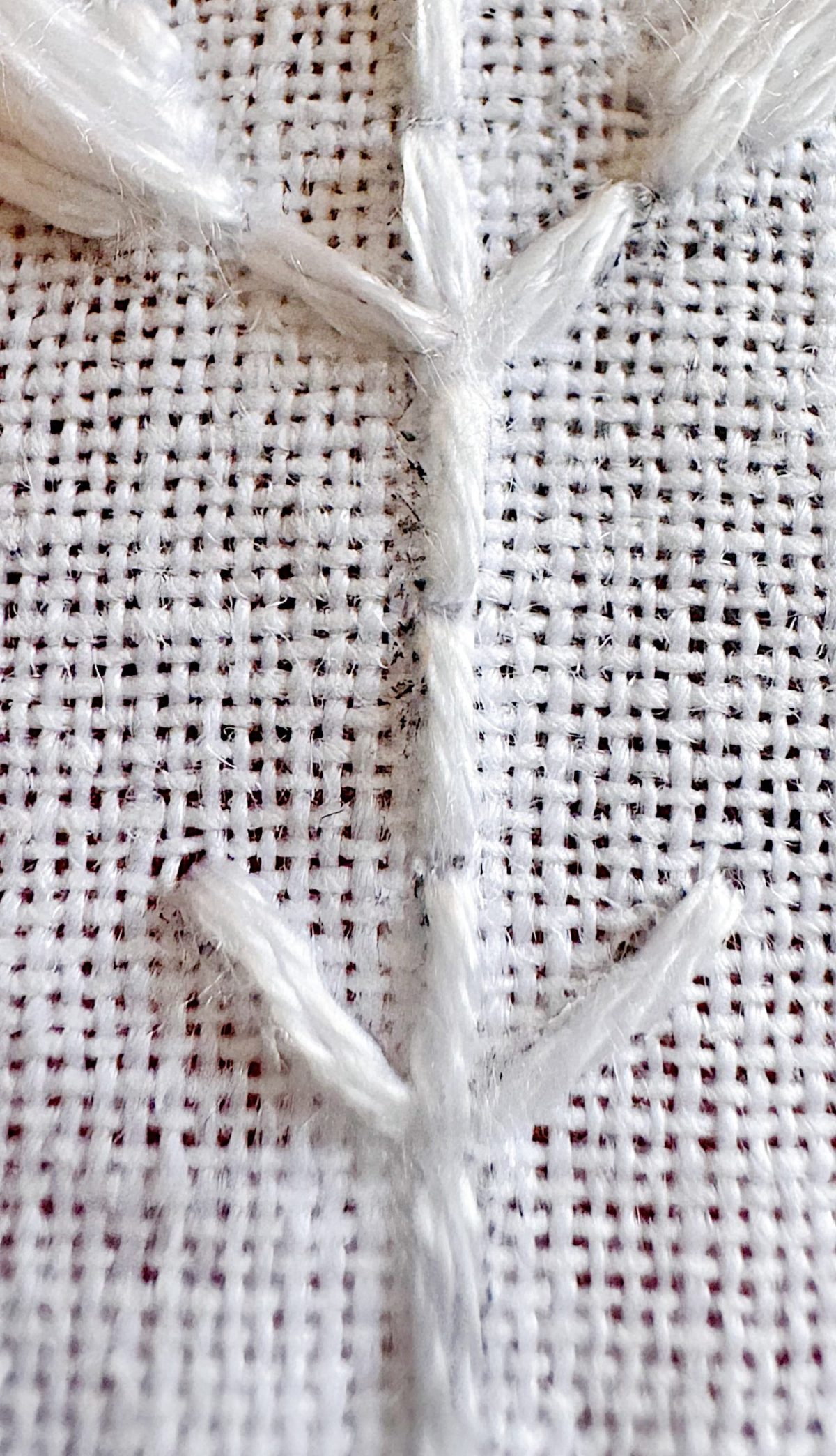 Close-up of a white embroidered pattern resembling a stem with branches on a coarse woven fabric background.