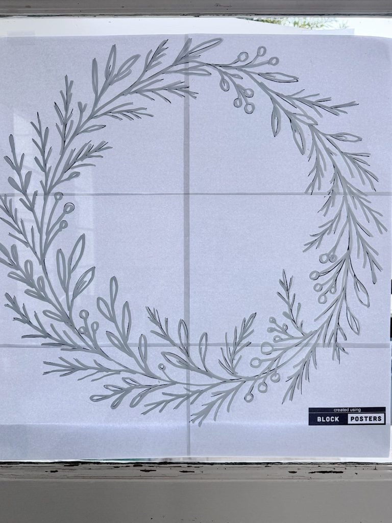 A grayscale botanical wreath design printed across four sheets of paper, assembled and taped to a window with a "Block Posters" label visible in the lower right corner.
