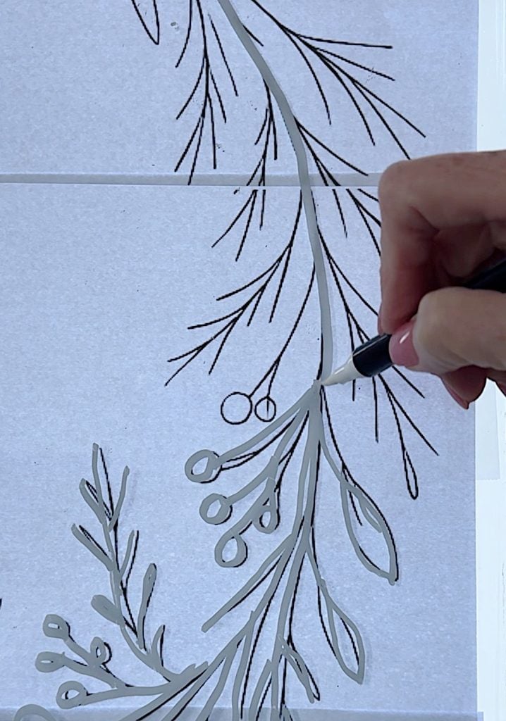 A hand is tracing over a botanical line drawing with a black marker on a white sheet of paper.