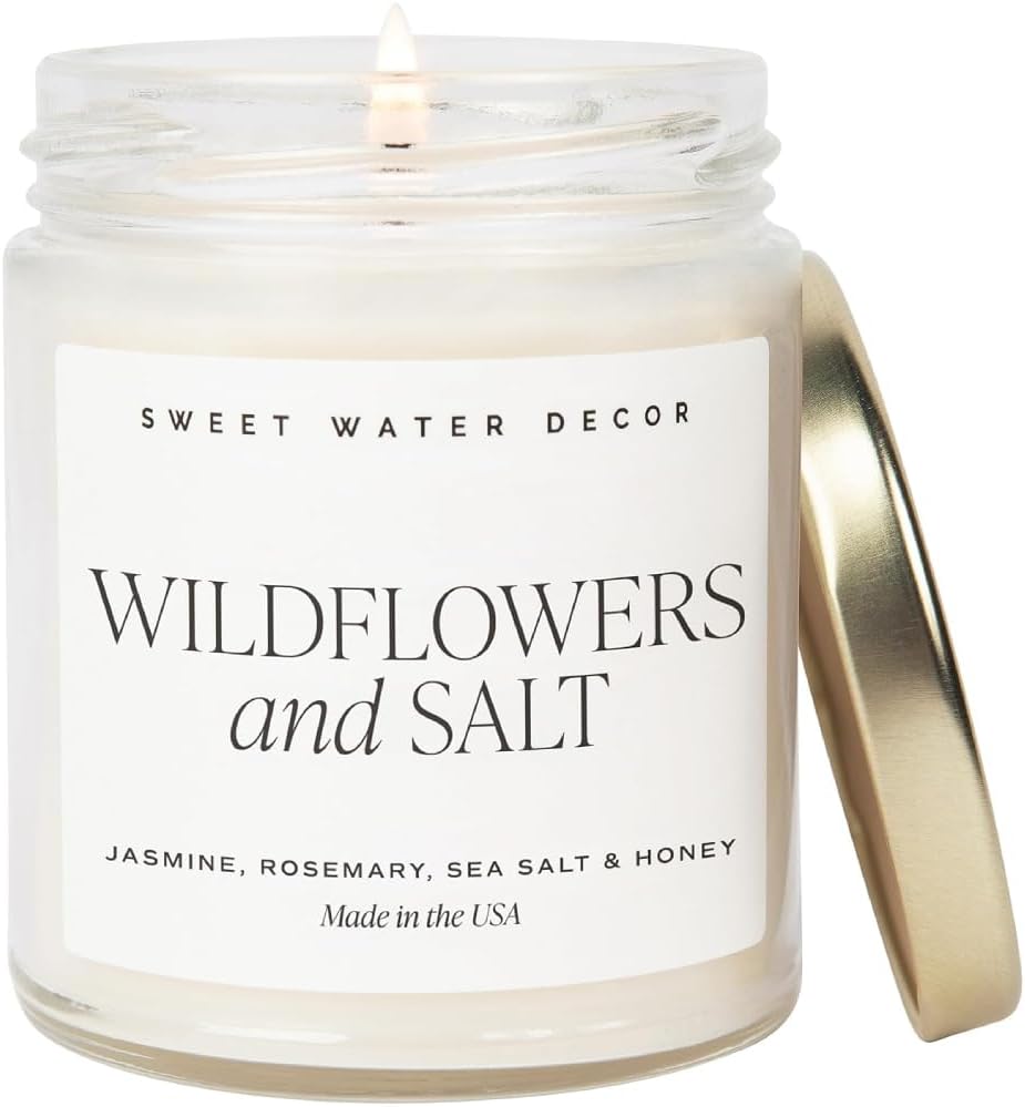 A lit candle in a glass jar labeled "Wildflowers and Salt" with the lid resting on the side.