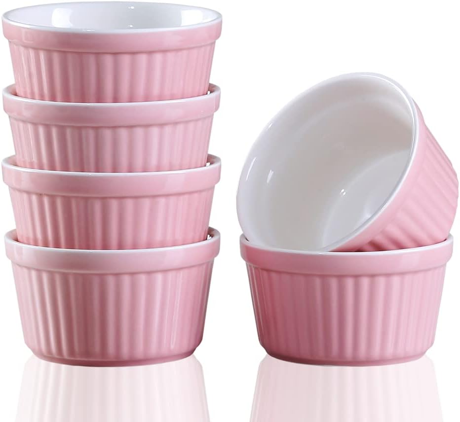 A stack of four pink ceramic ramekins with white interiors, next to two more ramekins, one upright and one on its side.