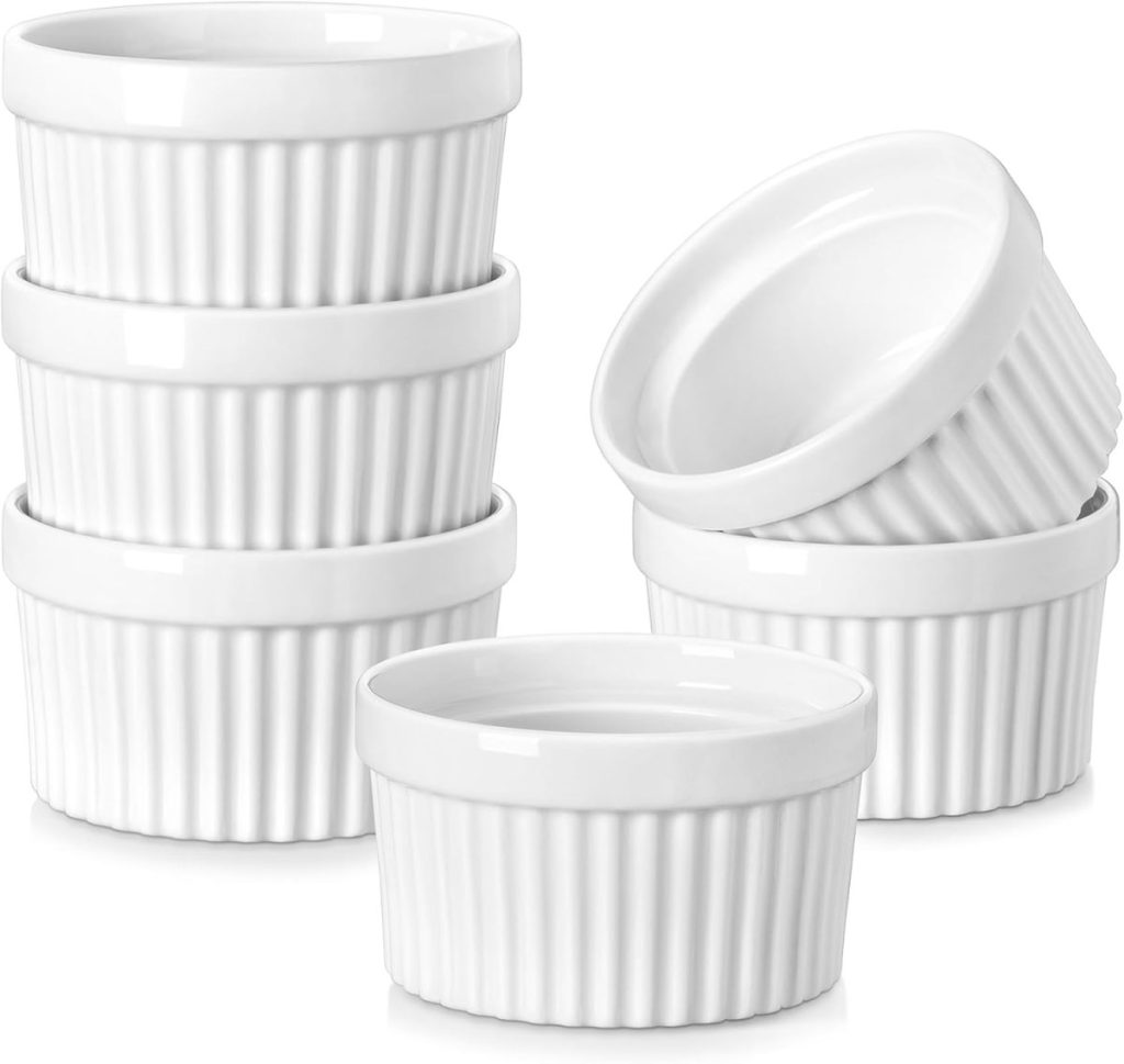 Six white ceramic ramekins, five stacked into two piles and one placed in front, on a plain white background.