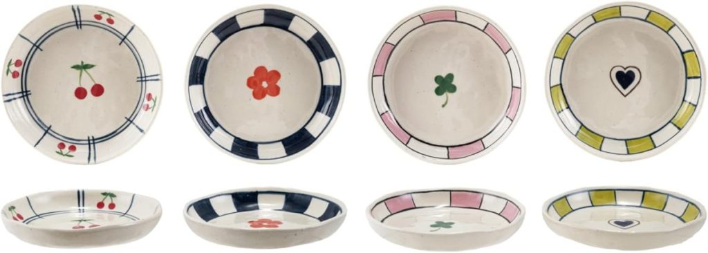 Eight ceramic plates with different patterns: cherries, red flower, green clover, and black heart, each bordered with blue, black, pink, or yellow geometric designs.