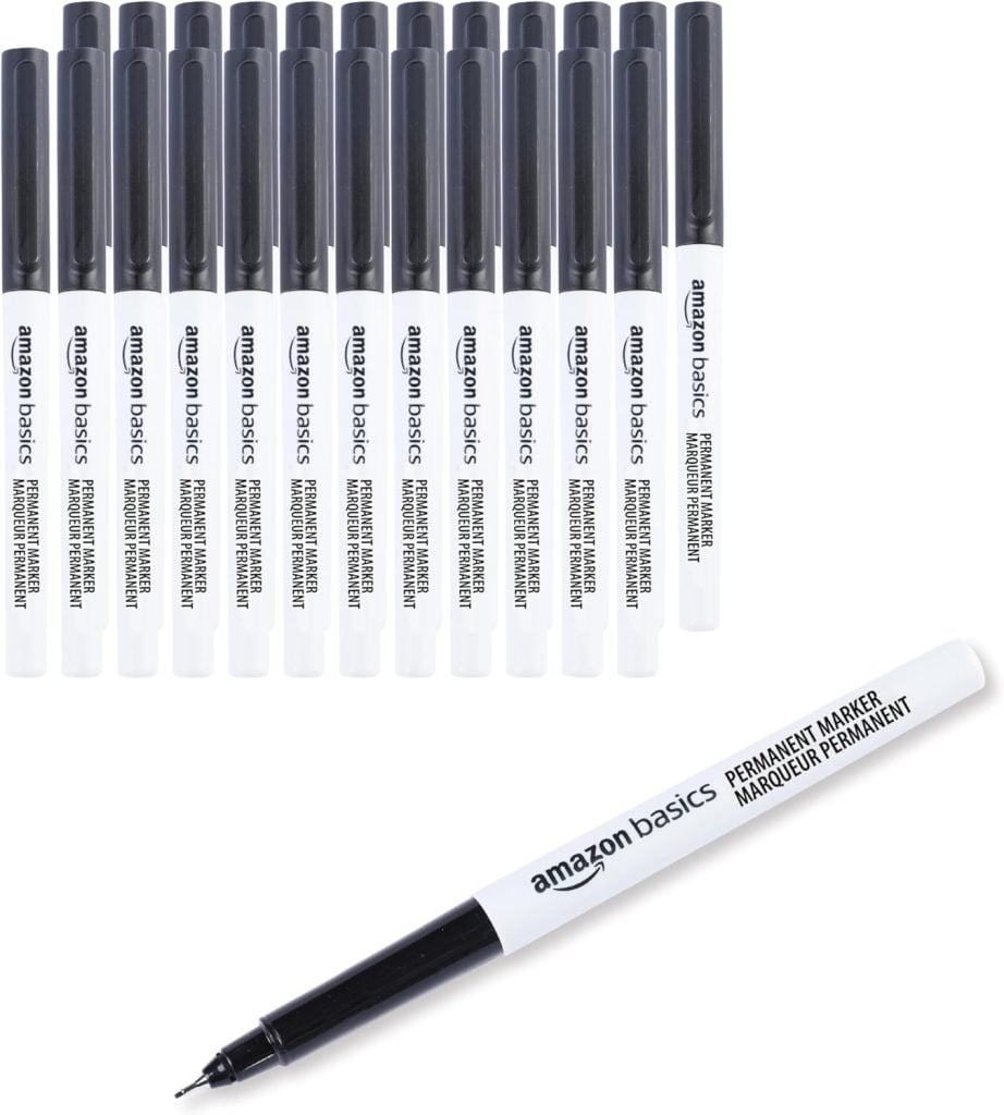 A set of sixteen Amazon Basics permanent markers with black caps and one marker shown separately with its cap off, revealing the fine tip.