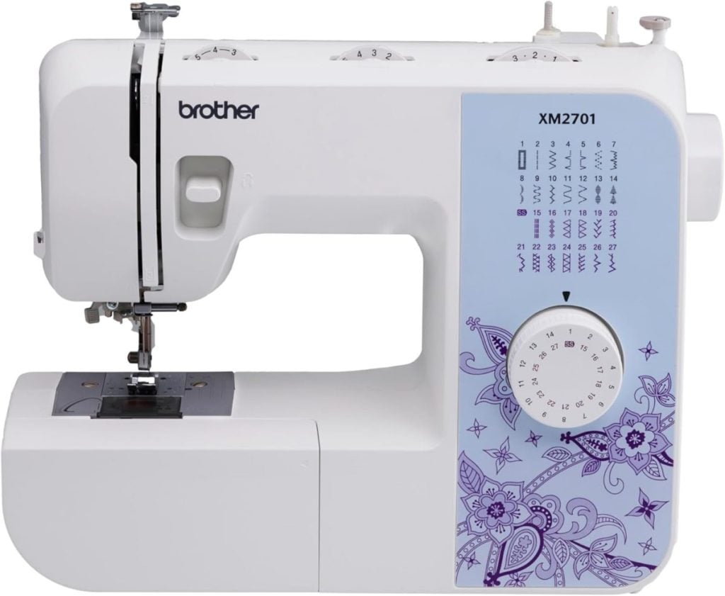 A Brother XM2701 sewing machine with a white body, blue panel, stitch selector dial, and floral decorative design.