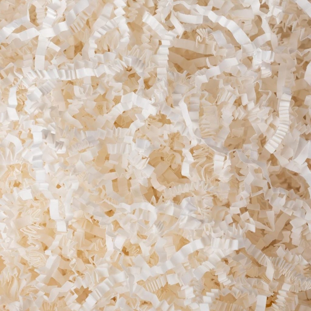 Close-up of a pile of white crinkle-cut paper shreds, commonly used as packing or gift box filler.