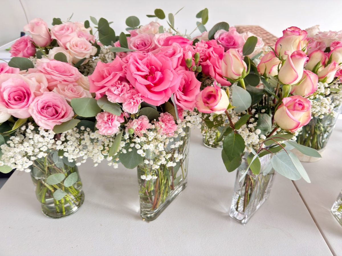 Several clear glass vases filled with pink roses, white baby's breath, greenery, and light pink carnations are arranged on a white surface.