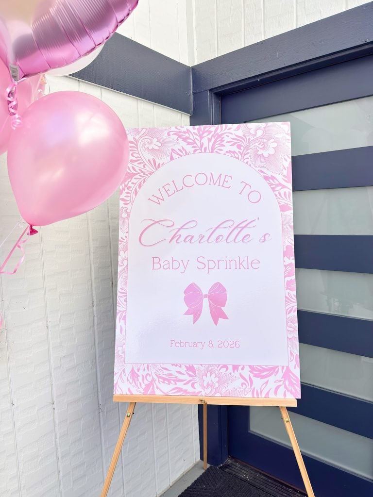 A large pink and white sign on an easel reads "Welcome to Charlotte's Baby Sprinkle, February 8, 2025," with pink balloons beside it.