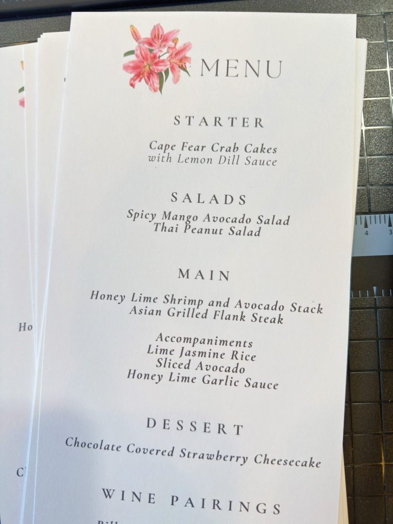 A printed menu featuring starter, salad, main, accompaniment, and dessert options, with a pink flower illustration at the top. A ruler is partially visible beside the menu.