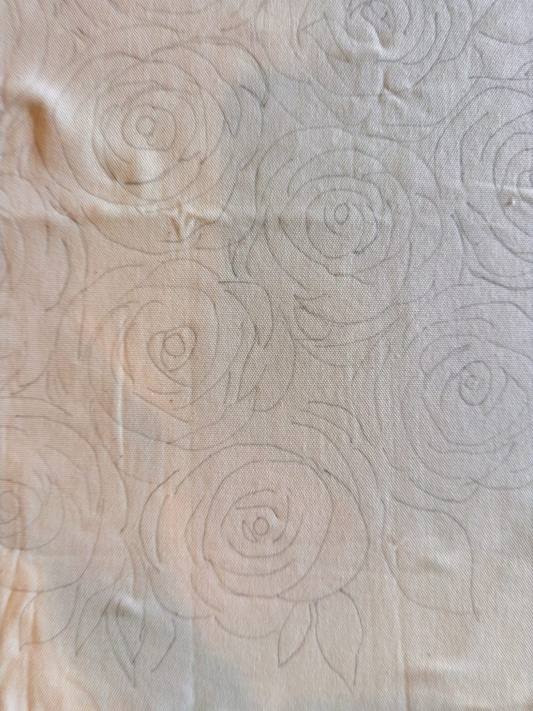 A beige fabric with a faint outline pattern of roses and leaves drawn across its surface.