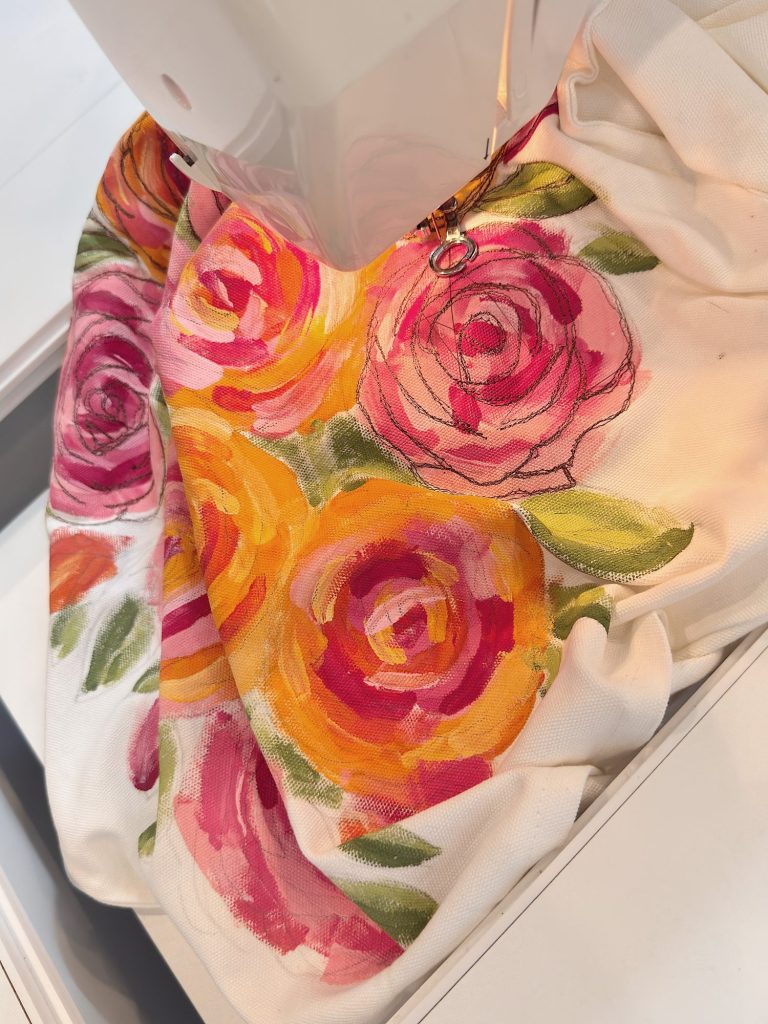 A sewing machine stitching a piece of fabric decorated with colorful painted roses and green leaves.