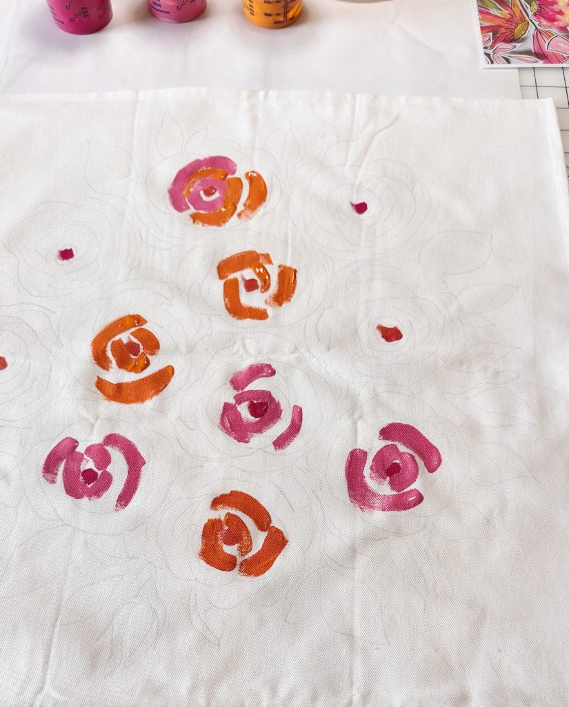 A white fabric with partially painted red and orange flower designs; outlines of additional flowers are visible in pencil.