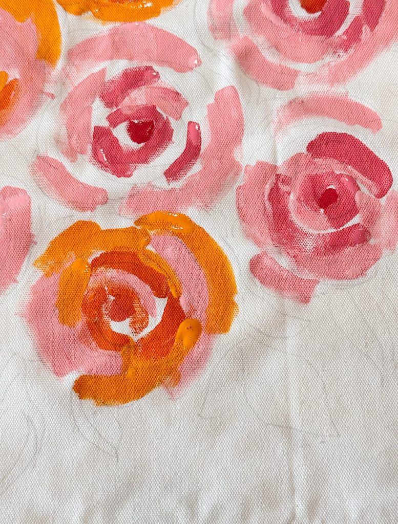 A fabric with a pattern of loosely painted pink and orange rose-like flowers on a white background.