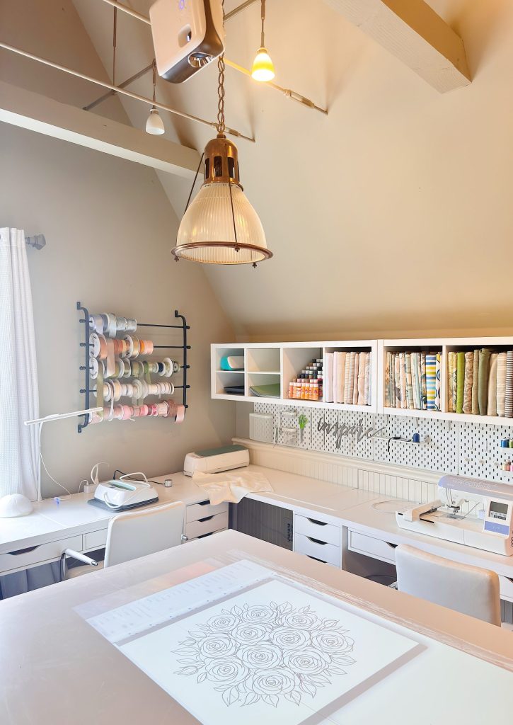 A well-organized craft room features shelves with fabric, a ribbon rack, a work table with a floral design sheet, and various craft supplies arranged neatly.