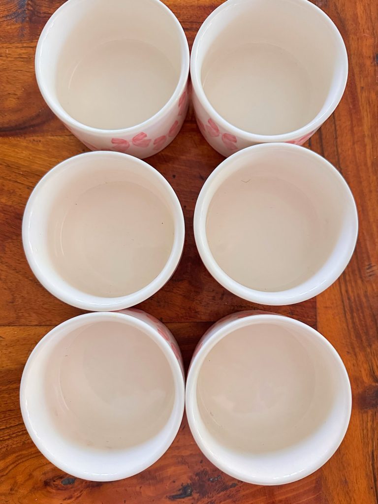 Six white ceramic cups arranged in two columns of three on a wooden surface, viewed from above.