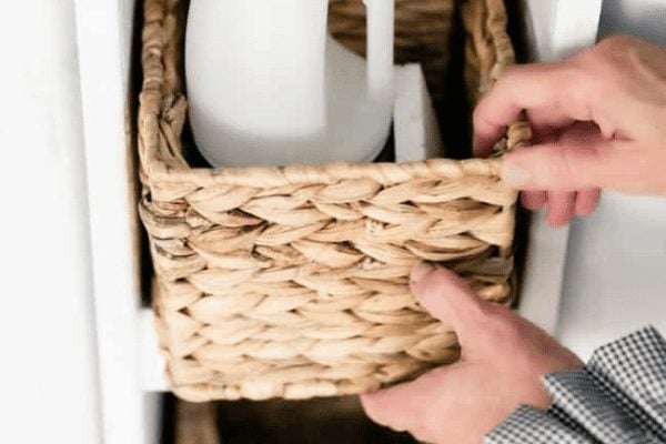 A person is sliding a woven basket into a white shelf, with part of a white object visible inside the basket.