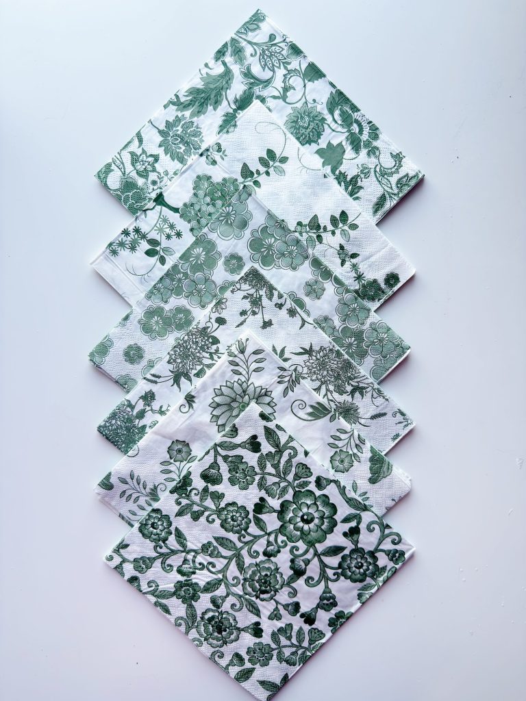 Five square napkins with green floral patterns are arranged in an overlapping, diamond-shaped layout on a white background.