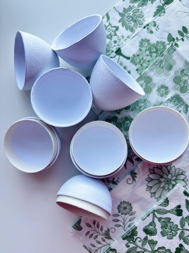 Several empty white egg shells are arranged on a surface next to green and white floral-patterned napkins.